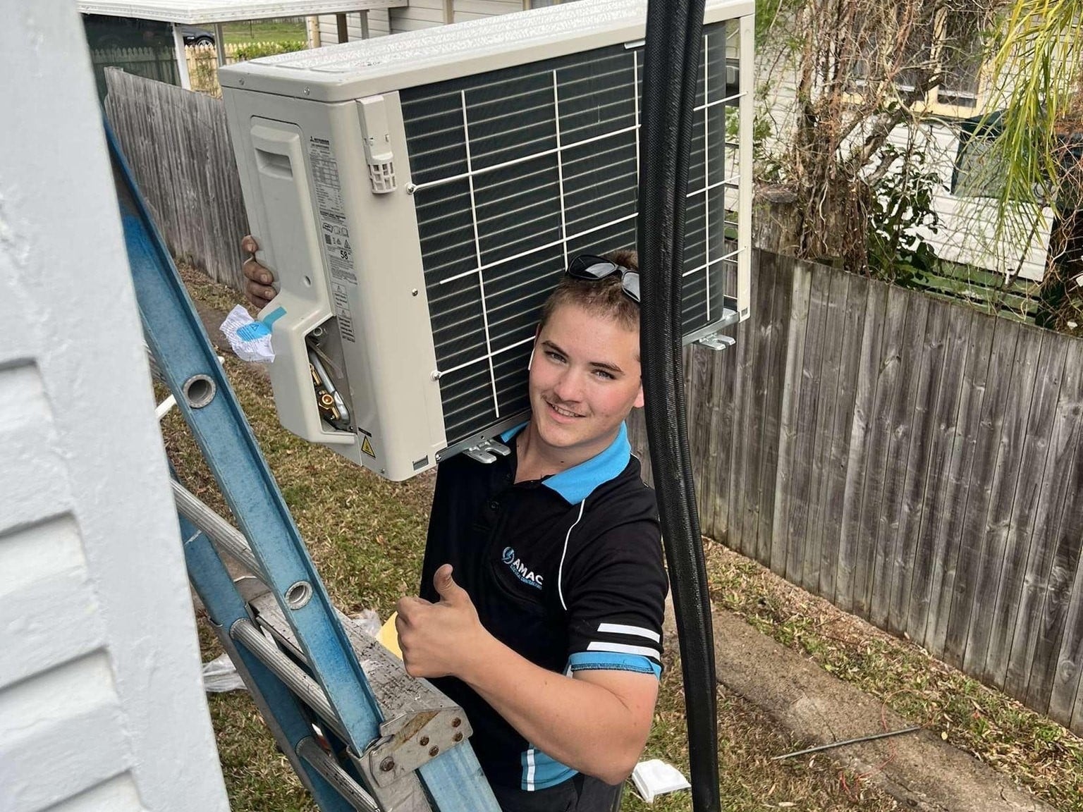 AMAC electrician with air conditioning unit on a ladder